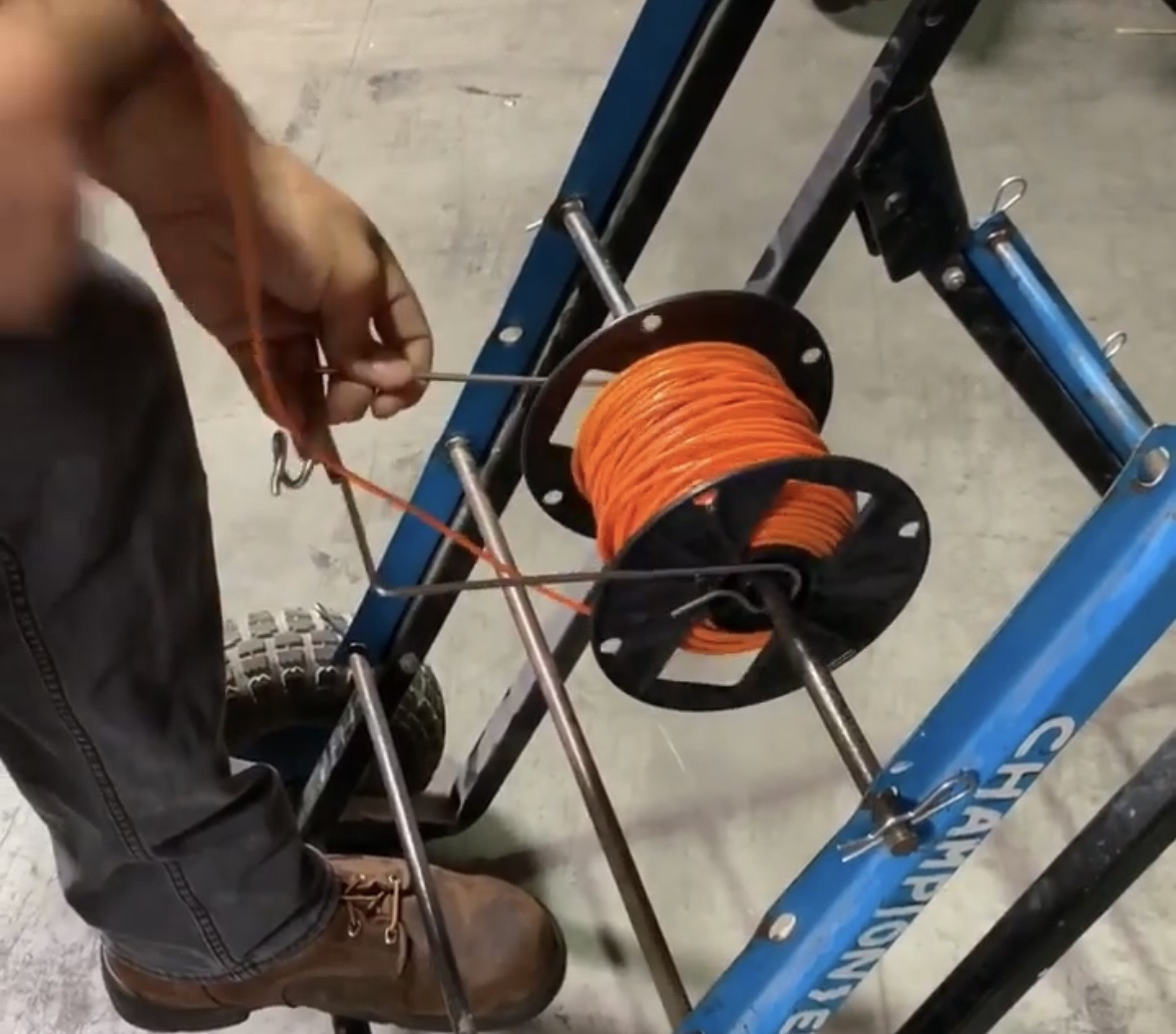 SpoolPig clipped onto a blue Champion wire caddy dispensing orange wire on a shop floor