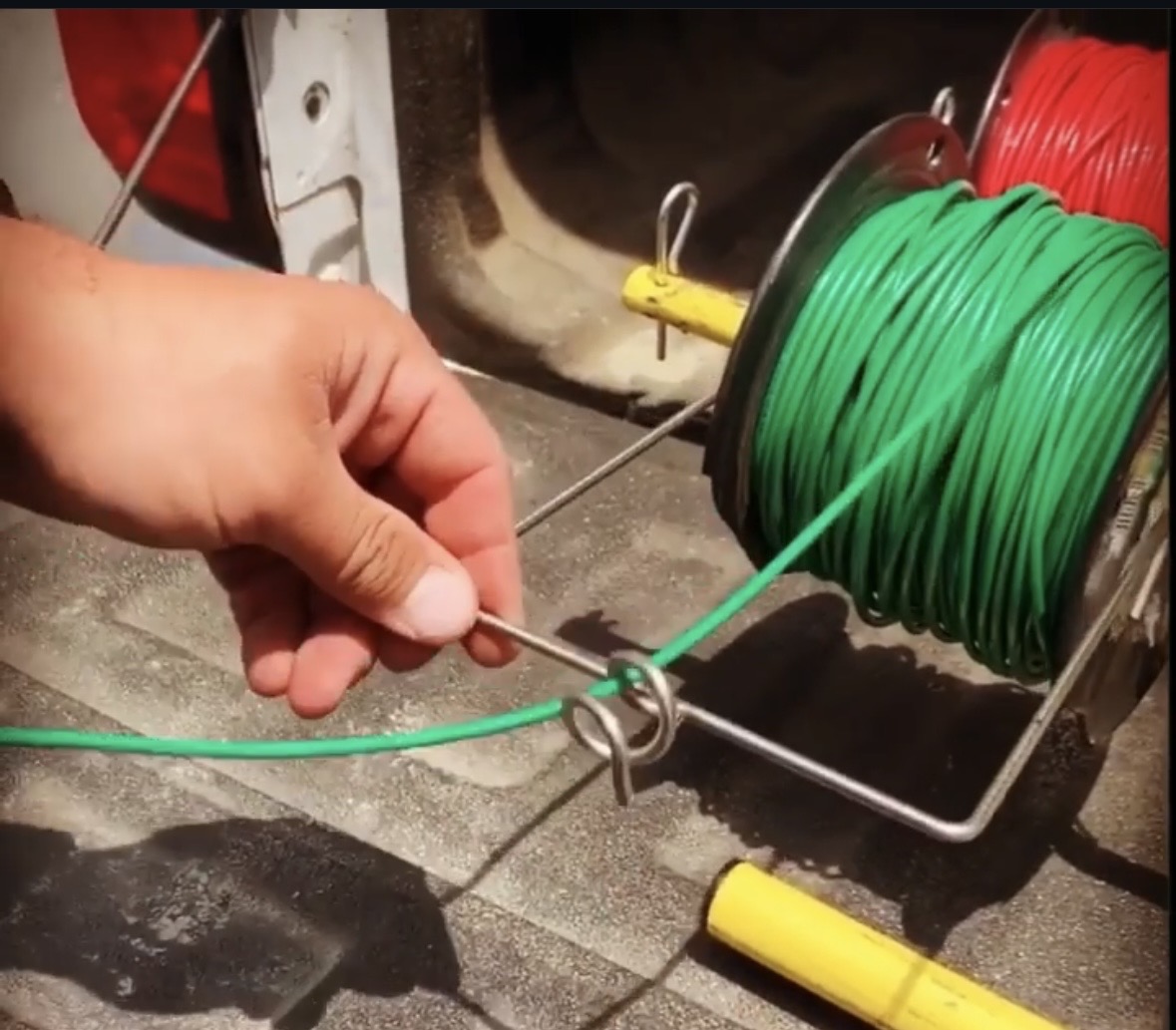 Electrician's hand feeding green THHN wire through the SpoolPig's Pig's Tail guide in a work van